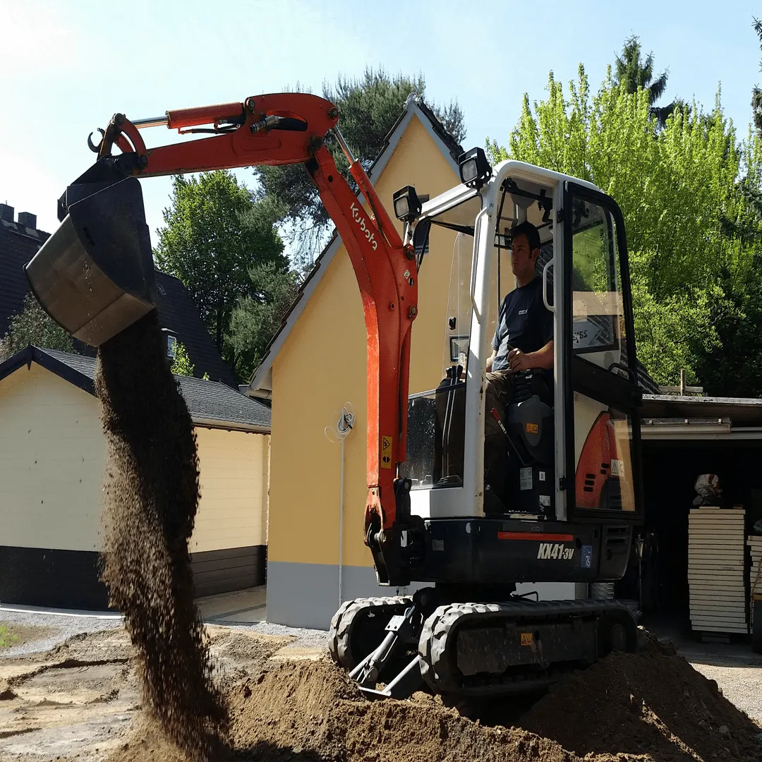 Kleibagger mit gelbem Ausleger beim Aushub neben einem Wohnhaus