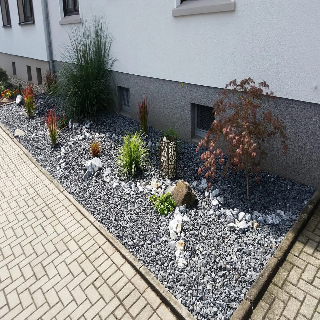Neu gestaltetes Pflanzenbeet mit Zierkies, Solitärgräsern und angrenzendem Pflasterweg